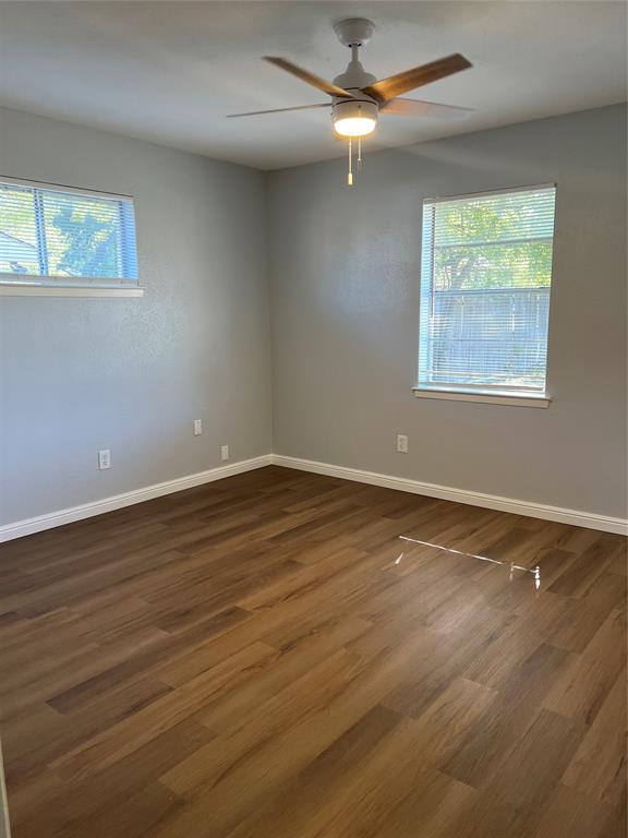 Room featuring wood-finish flooring, neutral walls, two windows, and a ceiling fan with integrated light fixture Room featuring wood-finish flooring, neutral walls, two windows, and a ceiling fan with integrated light fixture