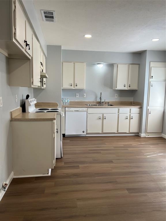 Kitchen featuring cabinetry with matte hardware, solid-surface countertops, wood-finish flooring, and recessed lighting