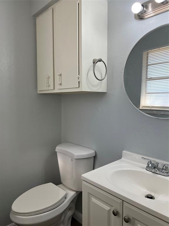 Bathroom featuring a white vanity cabinet with an integrated basin, brushed nickel hardware, a circular wall-mounted mirror, and a wall-mounted storage cabinet Bathroom featuring a white vanity cabinet with an integrated basin, brushed nickel hardware, a circular wall-mounted mirror, and a wall-mounted storage cabinet