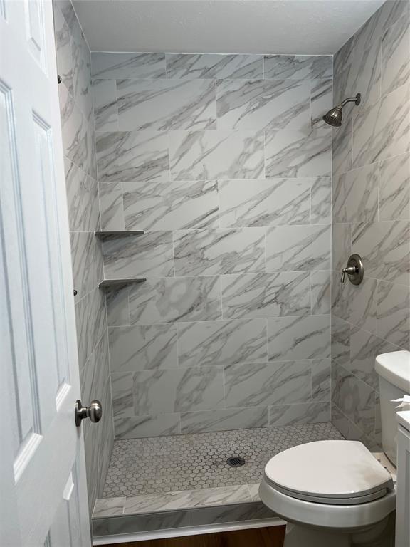 Shower enclosure featuring full-height large-format stone-patterned wall tile, hexagonal floor tile, two built-in corner shelves, and a metal shower head with matching pressure-balance valve Shower enclosure featuring full-height large-format stone-patterned wall tile, hexagonal floor tile, two built-in corner shelves, and a metal shower head with matching pressure-balance valve
