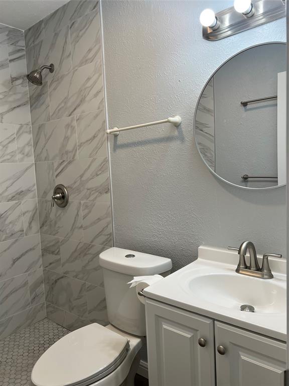 Bathroom featuring a walk-in shower with large-format tile surround, hexagonal floor tiling, white vanity with integrated sink, and round wall-mounted mirror Bathroom featuring a walk-in shower with large-format tile surround, hexagonal floor tiling, white vanity with integrated sink, and round wall-mounted mirror