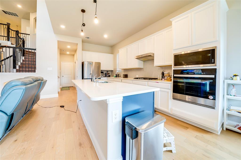 Kitchen with decorative backsplash, appliances with stainless steel finishes, light wood-type flooring, white cabinetry, and pendant lighting