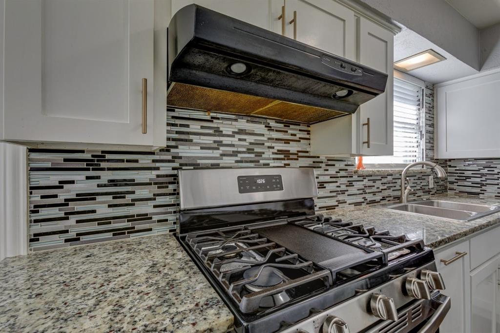 Kitchen featuring white cabinetry with brushed metal hardware, speckled stone countertops, a multi-tonal glass tile backsplash, and stainless steel gas range with a center griddle