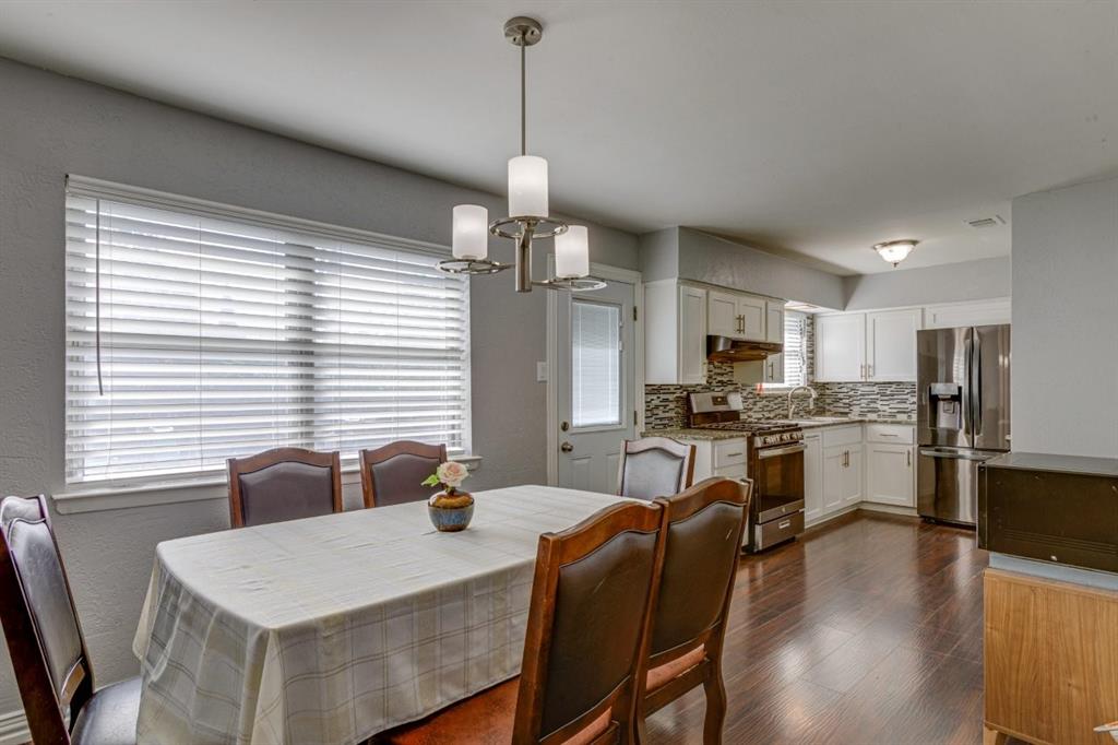 Kitchen featuring white cabinetry, wood-finish flooring, stainless steel appliances, multi-toned tile backsplash, and a three-light chandelier