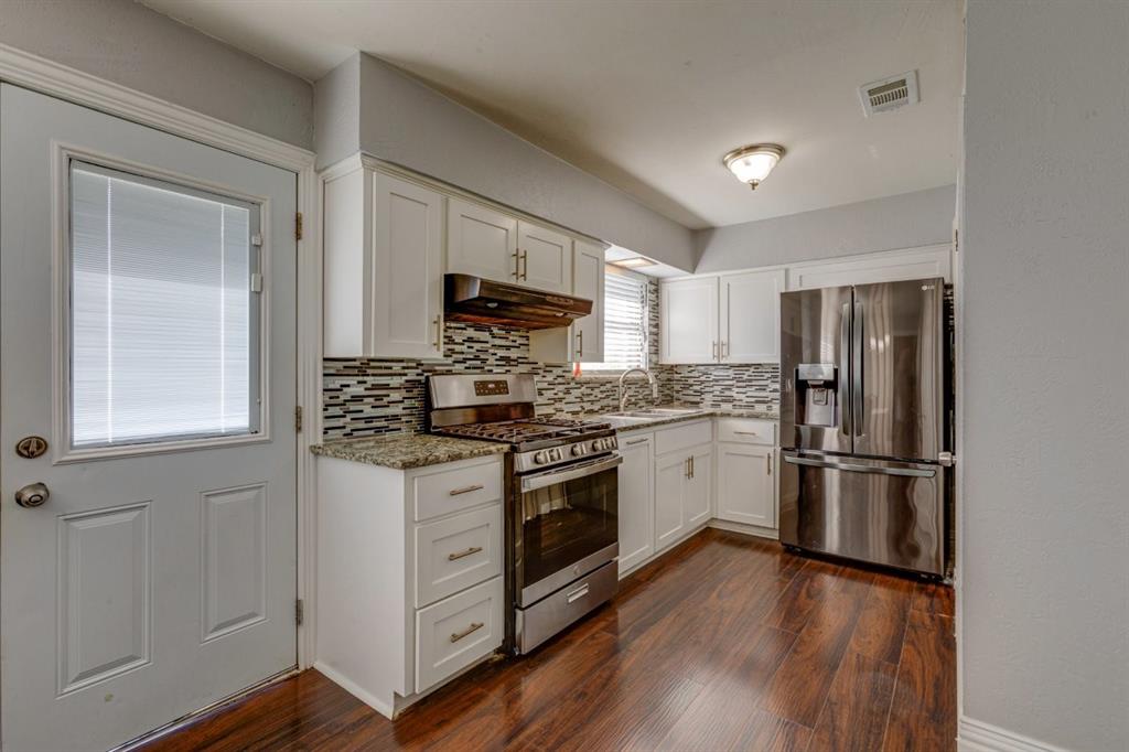 Kitchen featuring white shaker-style cabinetry, stone-finish countertops, decorative multi-tone tile backsplash, stainless steel appliances, and wood-finish flooring