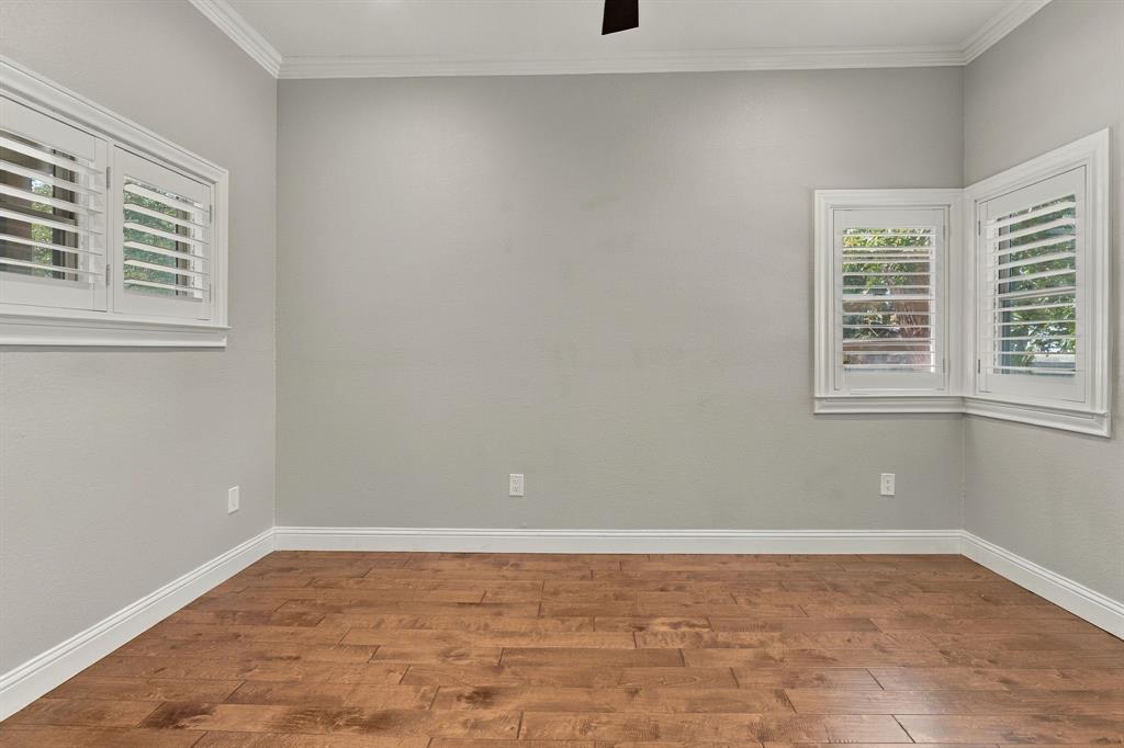 Wood-finish flooring, interior window shutters, neutral wall paint, crown molding, and a bay window configuration
