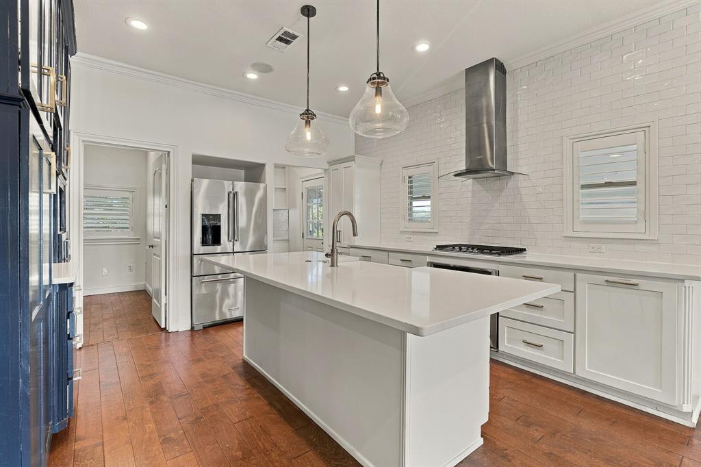 Kitchen featuring wood-finish flooring, a central island with a stone-finish countertop, stainless steel appliances, a white subway tile backsplash, and glass pendant lighting