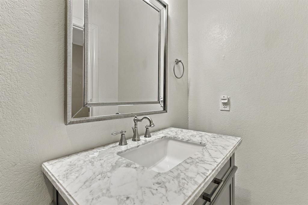 Stone-surface vanity featuring an undermount sink, brushed-metal widespread faucet, and rectangular framed mirror
