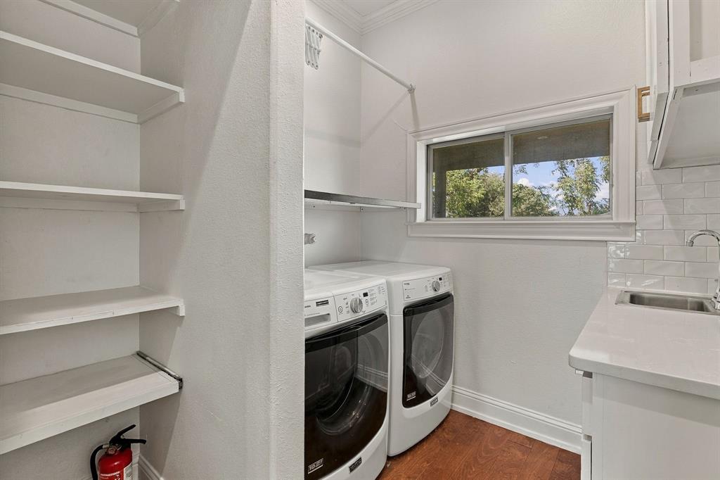 Laundry room featuring custom built-in shelving, a light-toned solid surface countertop, an undermount sink, subway tile backsplash, and wood-finish flooring