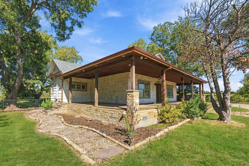 Stone veneer exterior featuring a wraparound covered porch, exposed wood ceiling beams, stone support columns, and a flagstone pathway
