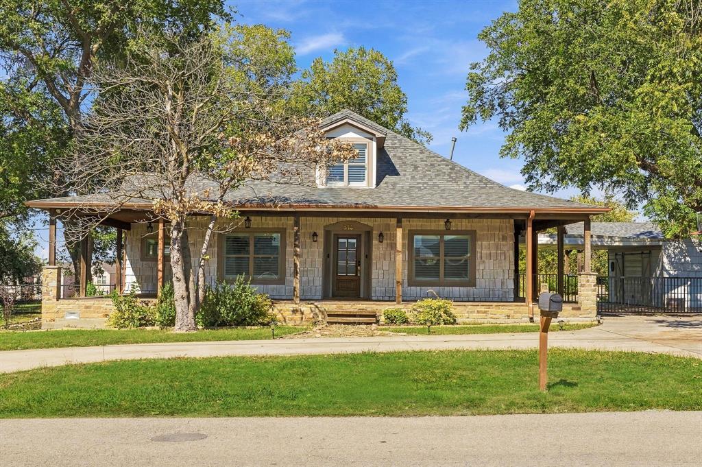 Single-story residence featuring a light-toned stone exterior, wrap-around covered porch, dormer window, and shingled roof