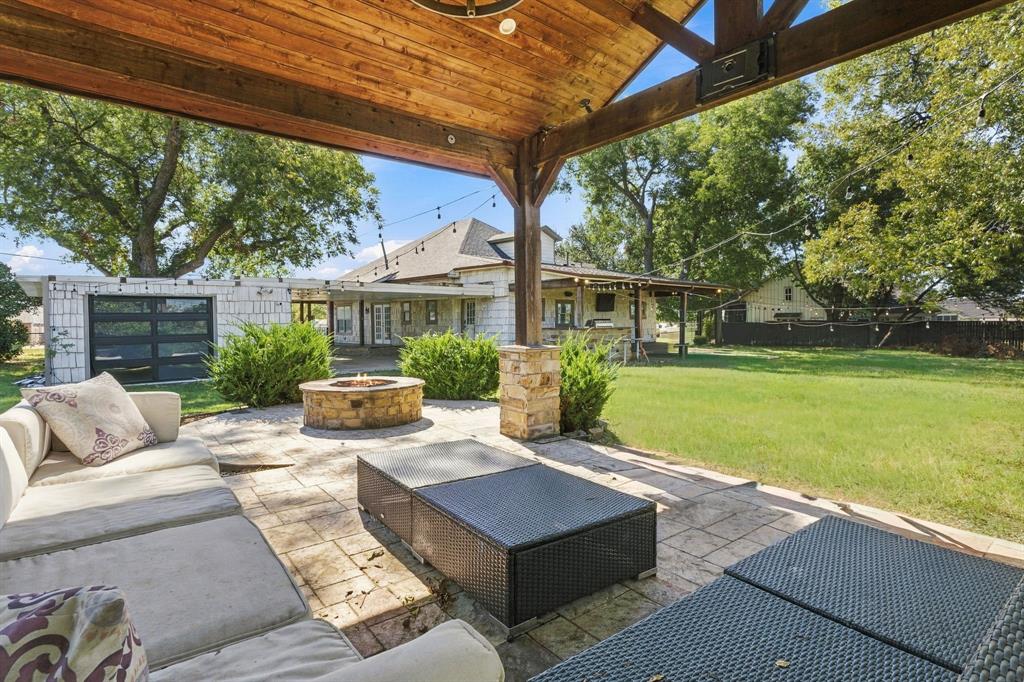 Covered patio featuring a timber-frame ceiling, stone-clad support columns, stone-finished fire pit, and stone-paver hardscaping