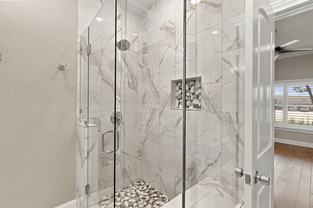 Walk-in shower featuring floor-to-ceiling large-format tile, glass enclosure, built-in recessed niche with decorative stone inlay, and a pebble-stone tiled floor