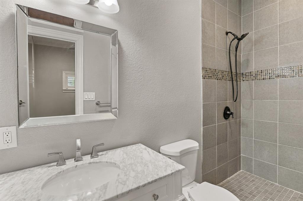 Bathroom featuring a vanity with a stone countertop and undermount sink, a framed mirror, and a tiled shower with a decorative mosaic inlay and a matte black handheld showerhead