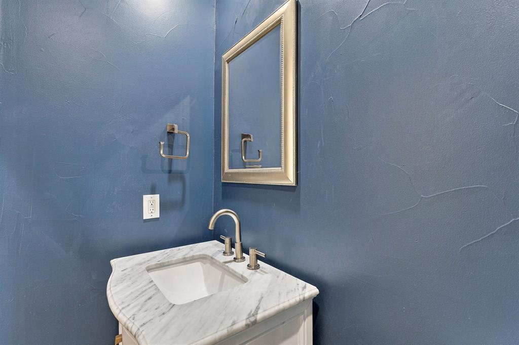Custom vanity with stone-top surface, undermount basin, brushed-nickel widespread faucet, framed wall-mounted mirror, and textured wall finish