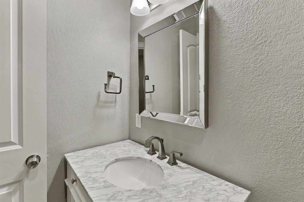 Vanity featuring a stone-surface countertop, integrated oval basin, polished metal widespread faucet, framed beveled-edge wall mirror, and dual-light fixture
