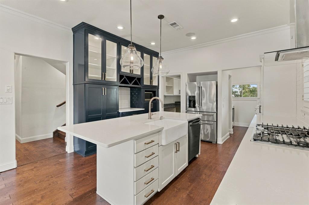 Kitchen featuring a central island with a farmhouse-style sink, white solid-surface countertops, floor-to-ceiling cabinetry with glass-front uppers, stainless steel appliances, and wood-finish flooring