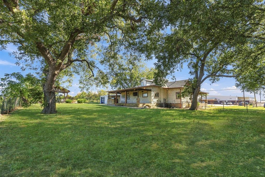 Stone exterior home featuring a covered front porch, expansive lawn, and mature trees