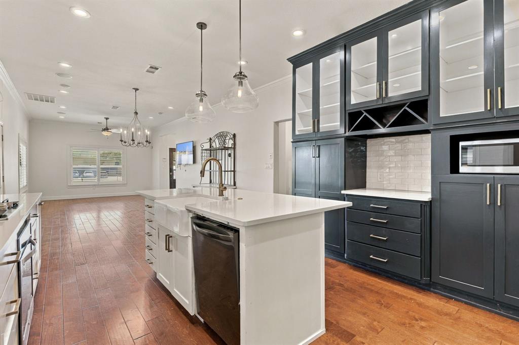 Kitchen featuring floor-to-ceiling dark cabinetry with glass-front uppers, a central island with a farmhouse sink, white stone countertops, subway tile backsplash, and wood-finish flooring
