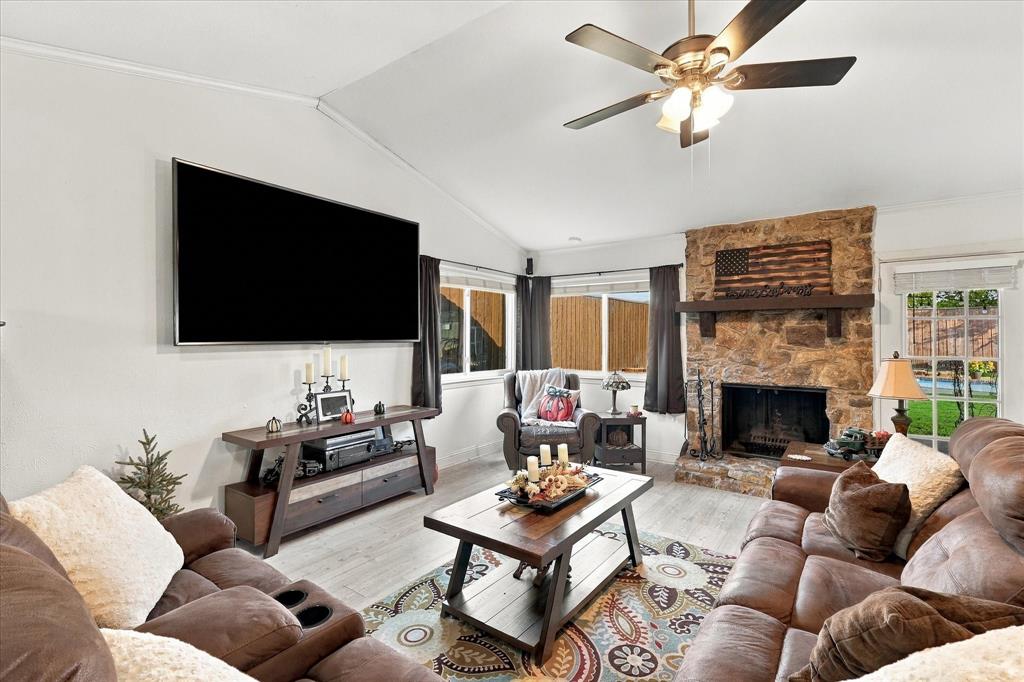 Vaulted ceiling, floor-to-ceiling stone fireplace, heavy timber mantel, wood-finish flooring, and ceiling fan
