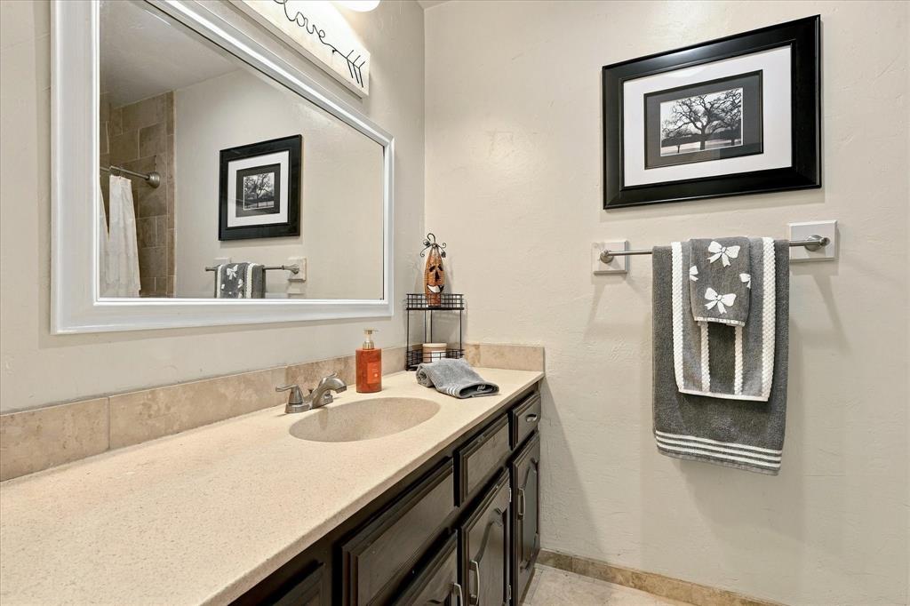 Wall-mounted mirror with a white frame, single-basin vanity with a stone-composite countertop, and stone-tile backsplash