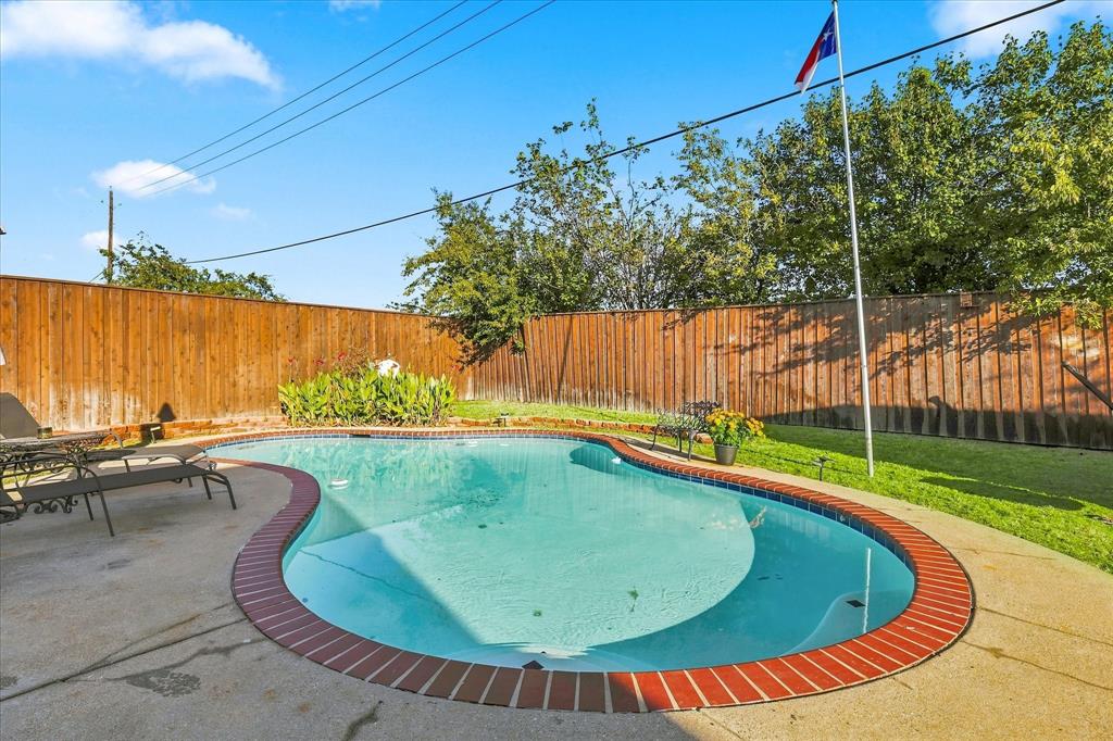 In-ground pool with brick coping, concrete patio, and fenced backyard