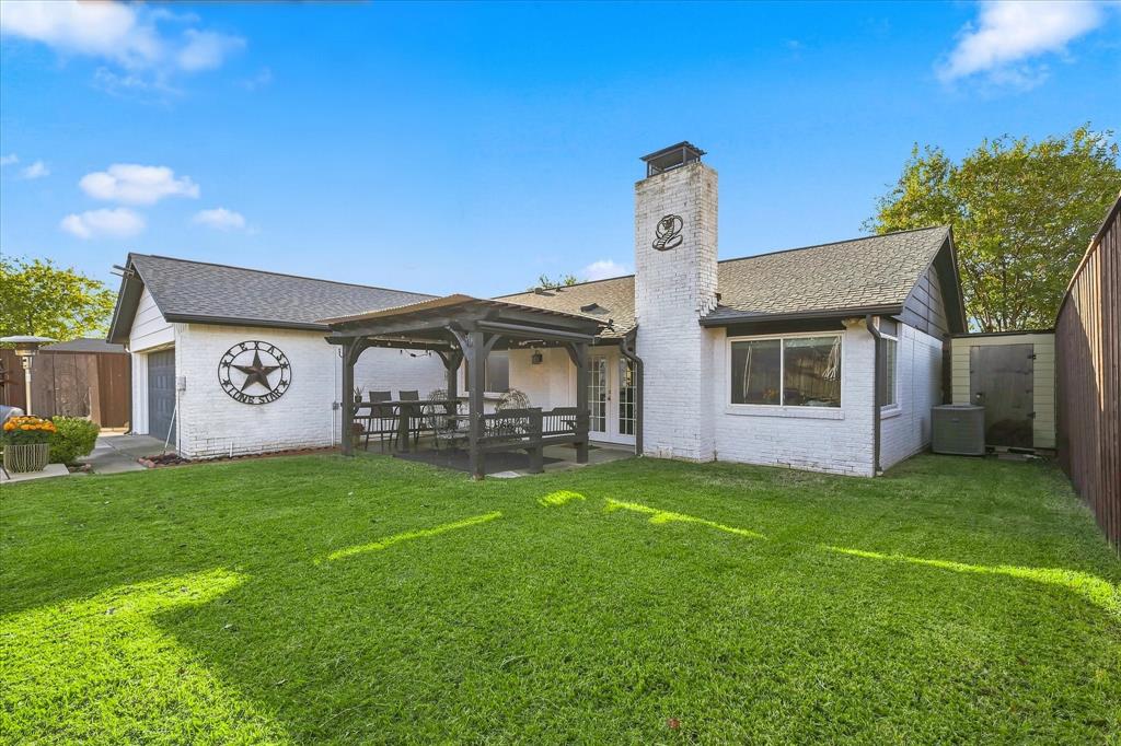 Fenced backyard featuring a manicured lawn, a covered timber pergola, a prominent masonry chimney, and white brick exterior finish