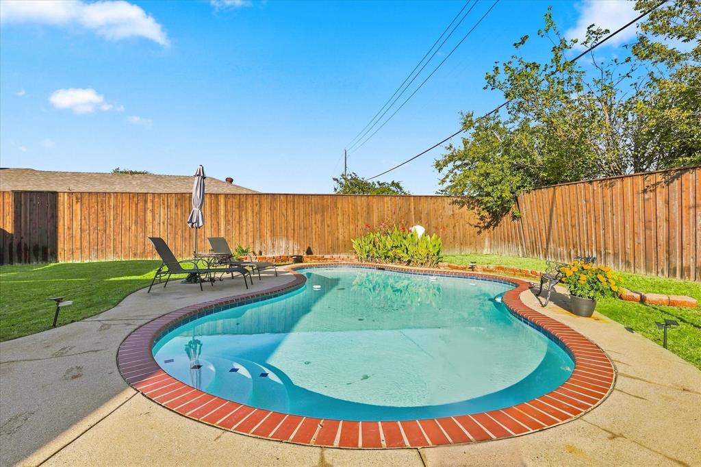 Free-form swimming pool with brick coping, concrete decking, and perimeter wood fencing