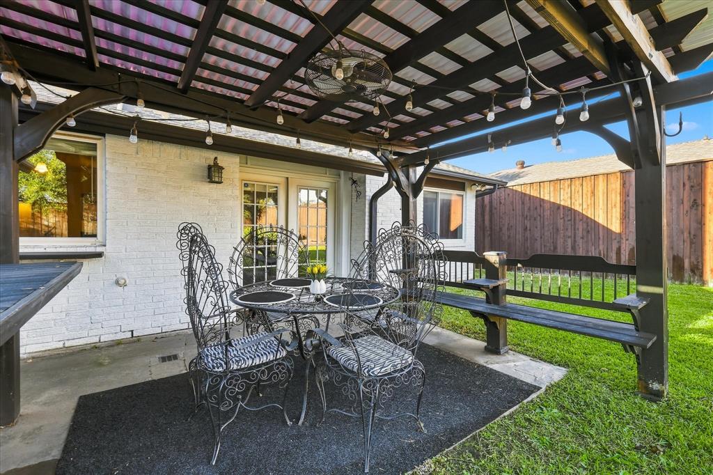 Covered patio featuring a timber pergola, built-in wooden bench seating, concrete flooring, and exterior wall-mounted lighting