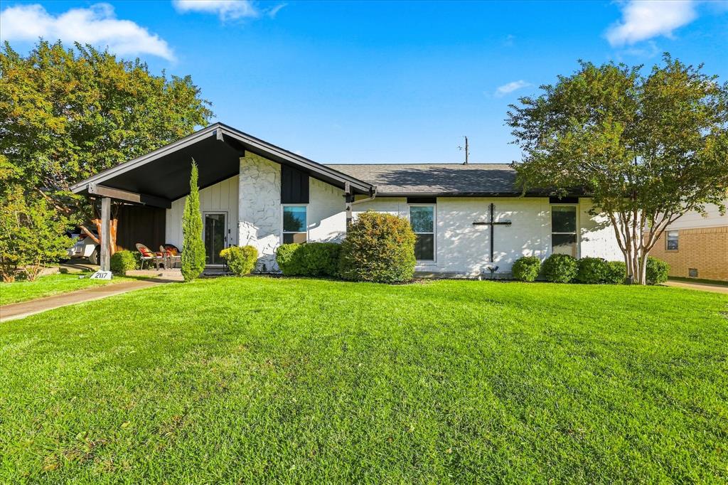 Mid-century modern architectural style featuring a painted brick exterior, a covered front porch, and an expansive front lawn with mature landscaping Mid-century modern architectural style featuring a painted brick exterior, a covered front porch, and an expansive front lawn with mature landscaping
