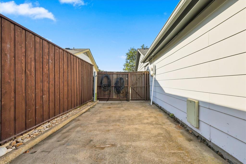 Concrete side yard featuring horizontal siding, a stained wood privacy fence, and a stone-lined border