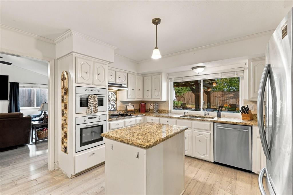Kitchen featuring white cabinetry, stone-surface countertops, center island, integrated wall ovens, and stainless steel dishwasher