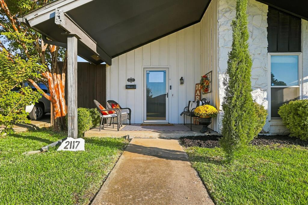 Covered front entryway featuring vertical siding, stone masonry accents, a concrete walkway, and an attached porch overhang