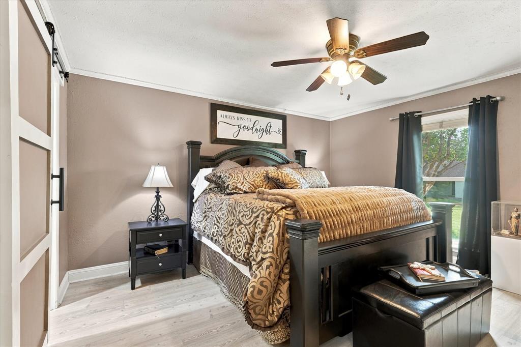 Neutral-toned walls featuring wood-finish flooring, a ceiling fan with integrated lighting, and a sliding barn-style door