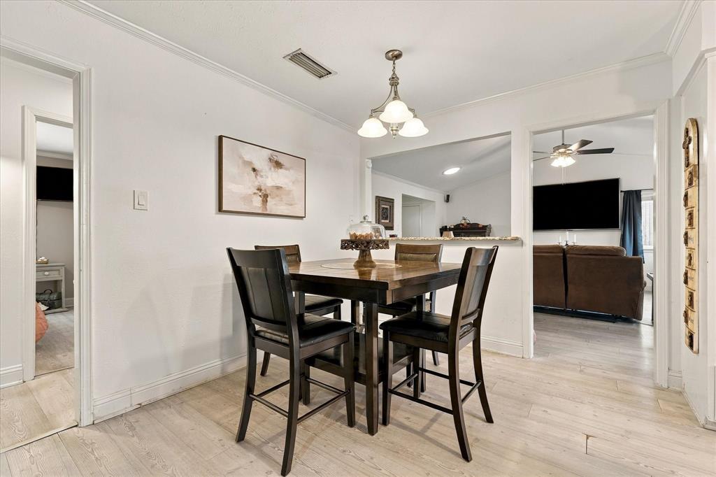 Dining area featuring light-toned wood-finish flooring, a multi-light pendant fixture, and a pass-through wall opening with a stone-top counter