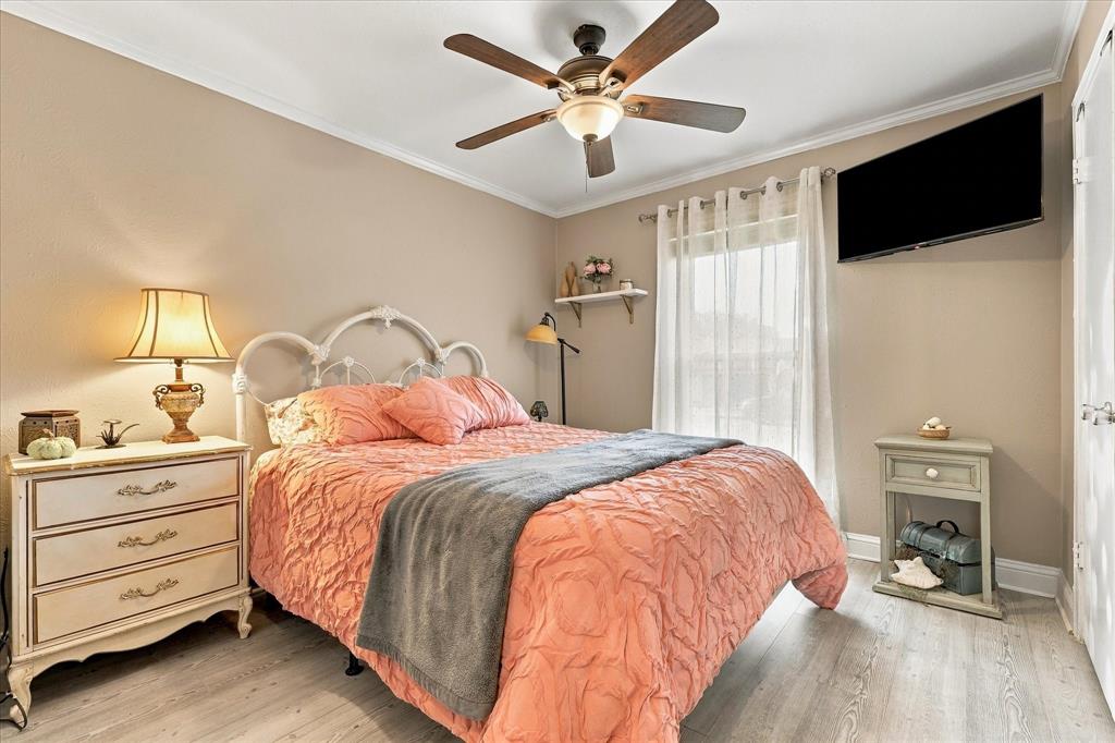 Wood-finish flooring, ceiling fan with integrated light fixture, window with sheer drapery, and a wall-mounted shelf