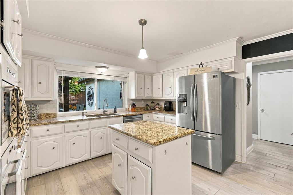Kitchen featuring white cabinetry, stone-surface countertops, central island, stainless steel refrigerator, and wood-finish flooring