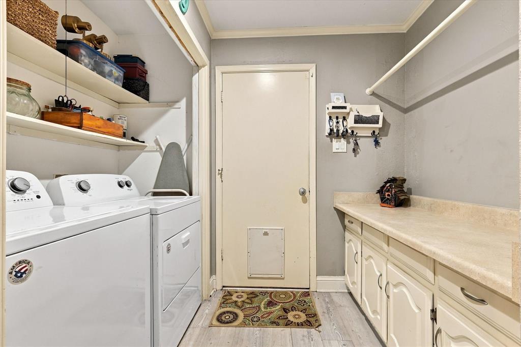 Laundry room featuring wood-finish flooring, white cabinetry with countertops, open shelving, and a door with a built-in pet portal