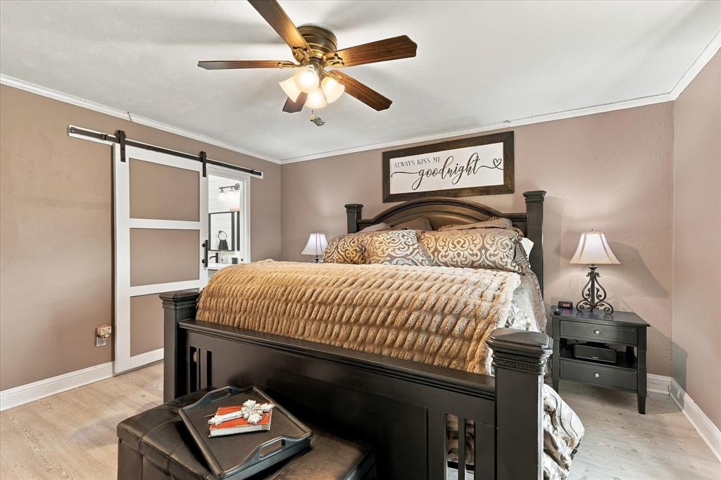 Wood-finish flooring, sliding barn door with black hardware, and a ceiling fan with integrated lighting