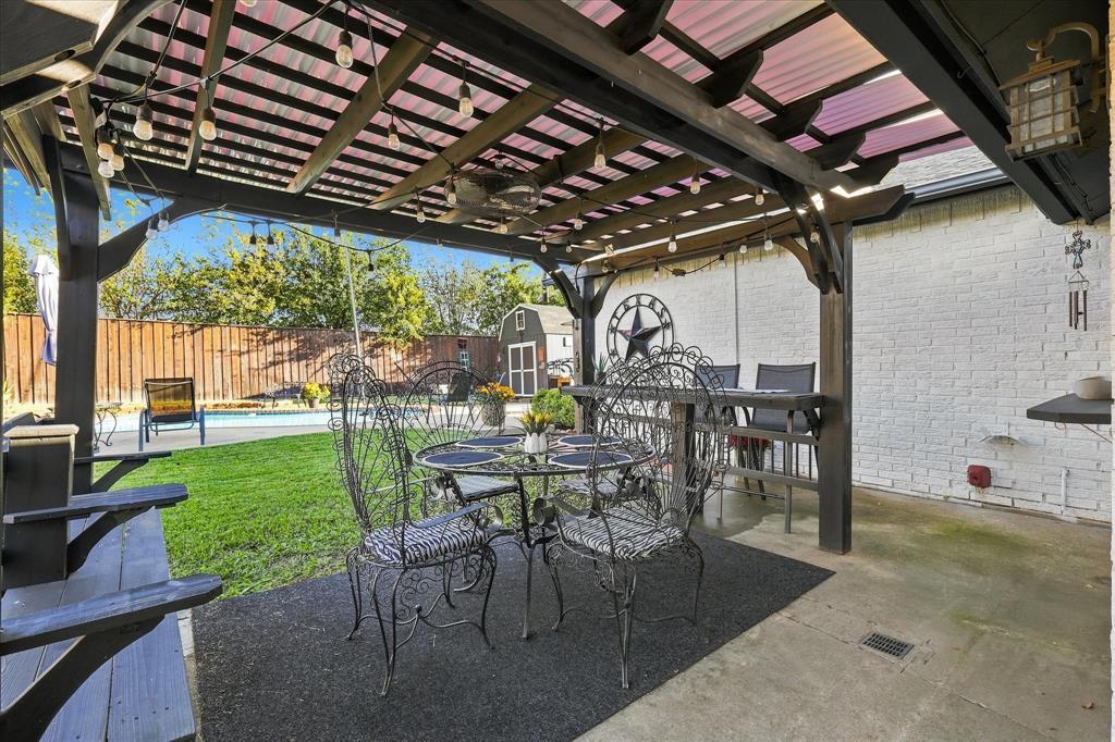 Covered outdoor pergola featuring a wooden timber frame, integrated ceiling fan, and painted brick exterior wall