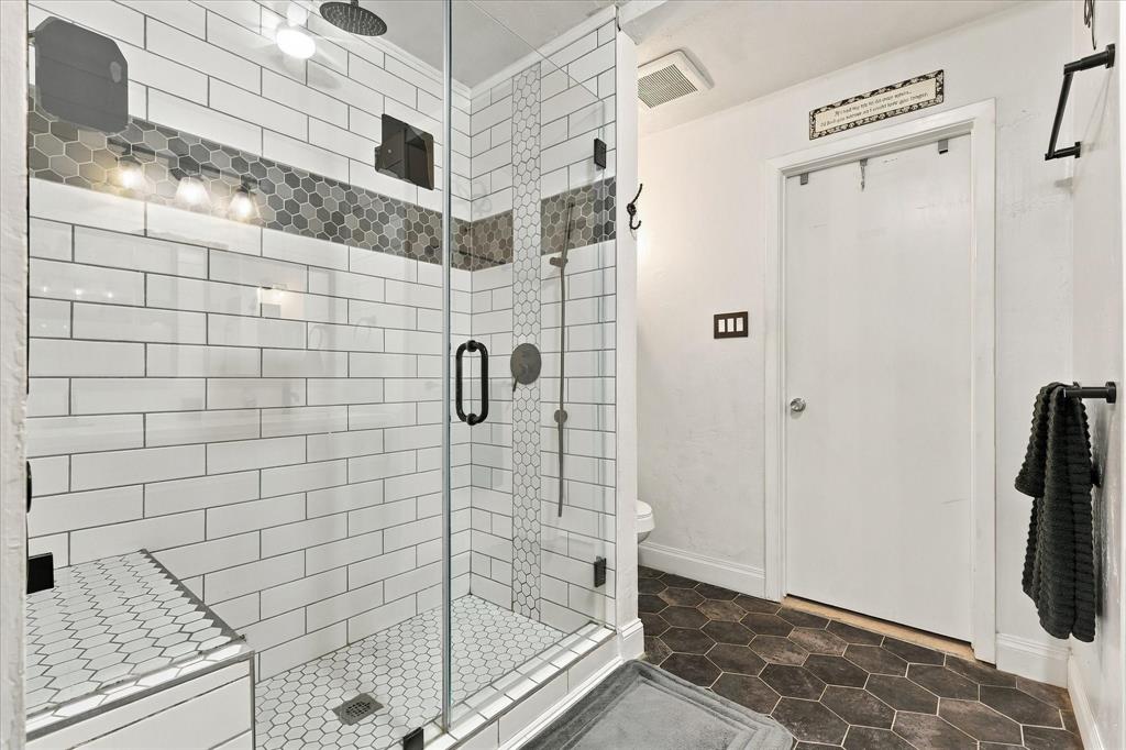 Walk-in shower featuring a glass enclosure, rainfall showerhead, white subway tile walls, and decorative hexagonal tile accents with a coordinating hexagonal floor tile