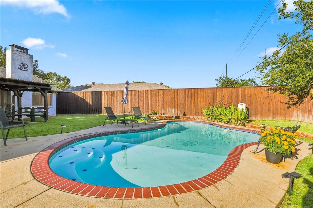 Backyard featuring an in-ground swimming pool with brick coping, concrete patio, covered patio structure, and perimeter wood privacy fencing