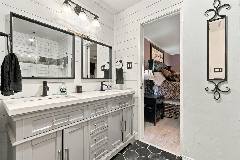 Double vanity featuring a white composite countertop, undermount sinks, matte black fixtures, shiplap wall accents, and hexagonal floor tiling