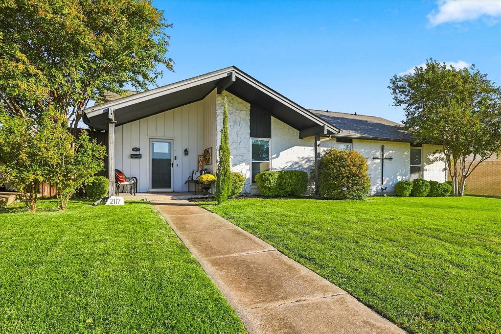 Mid-century modern architectural style featuring a low-pitched gable roof, board-and-batten siding, textured masonry facade, and an elongated concrete walkway