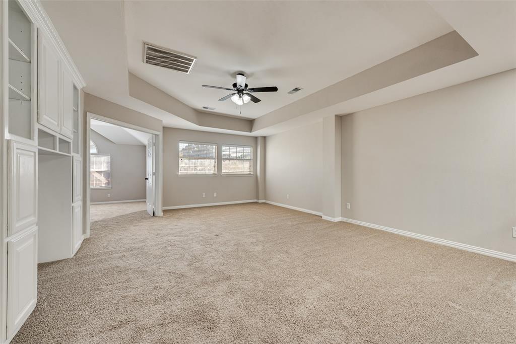 Room featuring a tray ceiling, built-in white cabinetry, wall-to-wall carpeting, and a ceiling fan with integrated lighting
