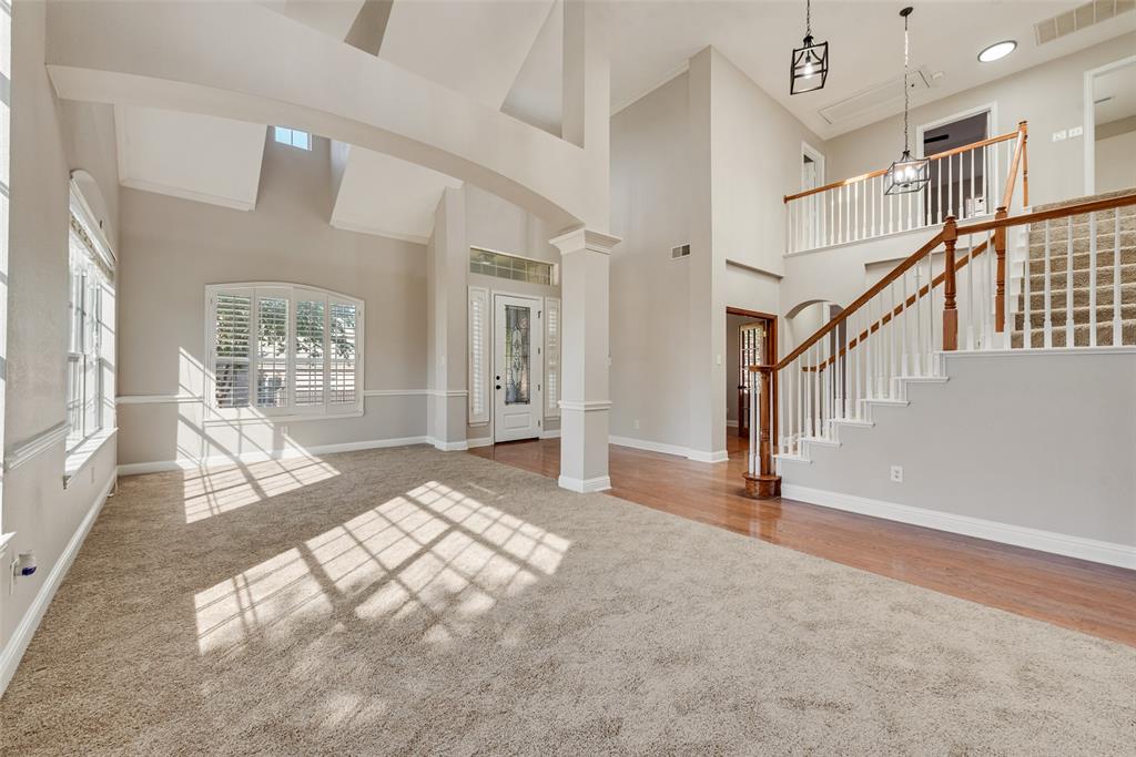 High-ceiling interior featuring arched architectural columns, a staircase with a wooden handrail and balusters, wood-finish flooring, and arched window detailing