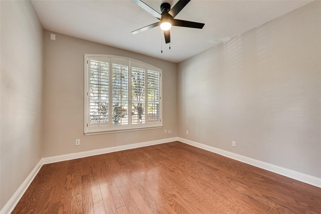 Room featuring wood-finish flooring, an arched window with plantation shutters, and a matte black ceiling fan with an integrated light fixture