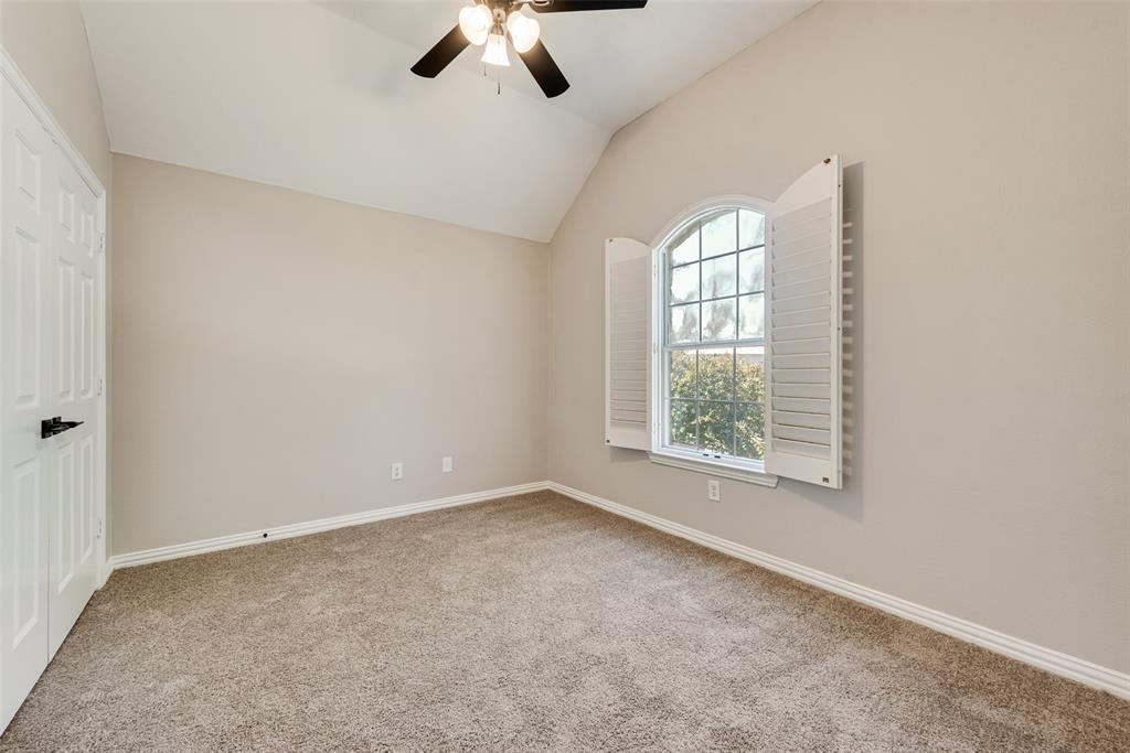 Vaulted ceiling room featuring neutral carpeting, arched window with white louvered shutters, and ceiling fan with integrated lighting