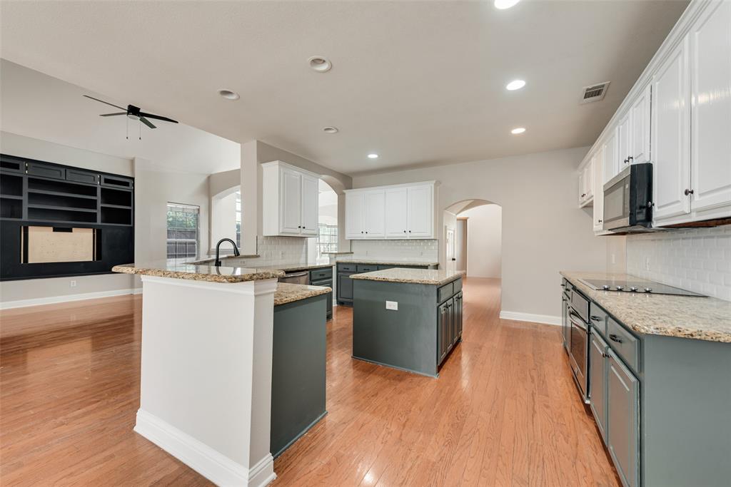 Kitchen featuring two-tone cabinetry, stone countertops, subway tile backsplash, built-in black shelving unit, and wood-finish flooring