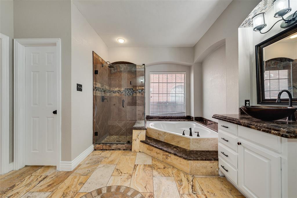 Bathroom featuring stone-tile flooring, a jetted soaking tub with a tiled surround, a glass-enclosed shower with decorative inlay, and a vanity with a vessel sink